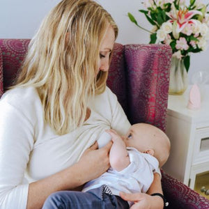 Mother feeding baby while using lactation massager for treatment for clogged duct