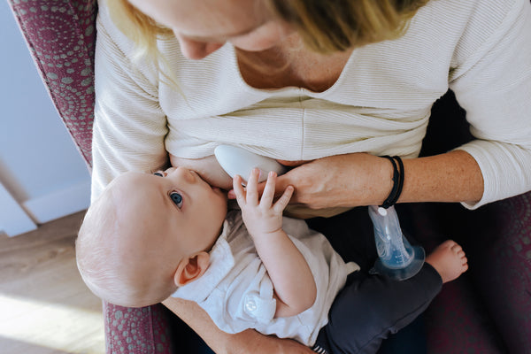 Child breastfeeding while massager is used as a clogged milk duct treatment